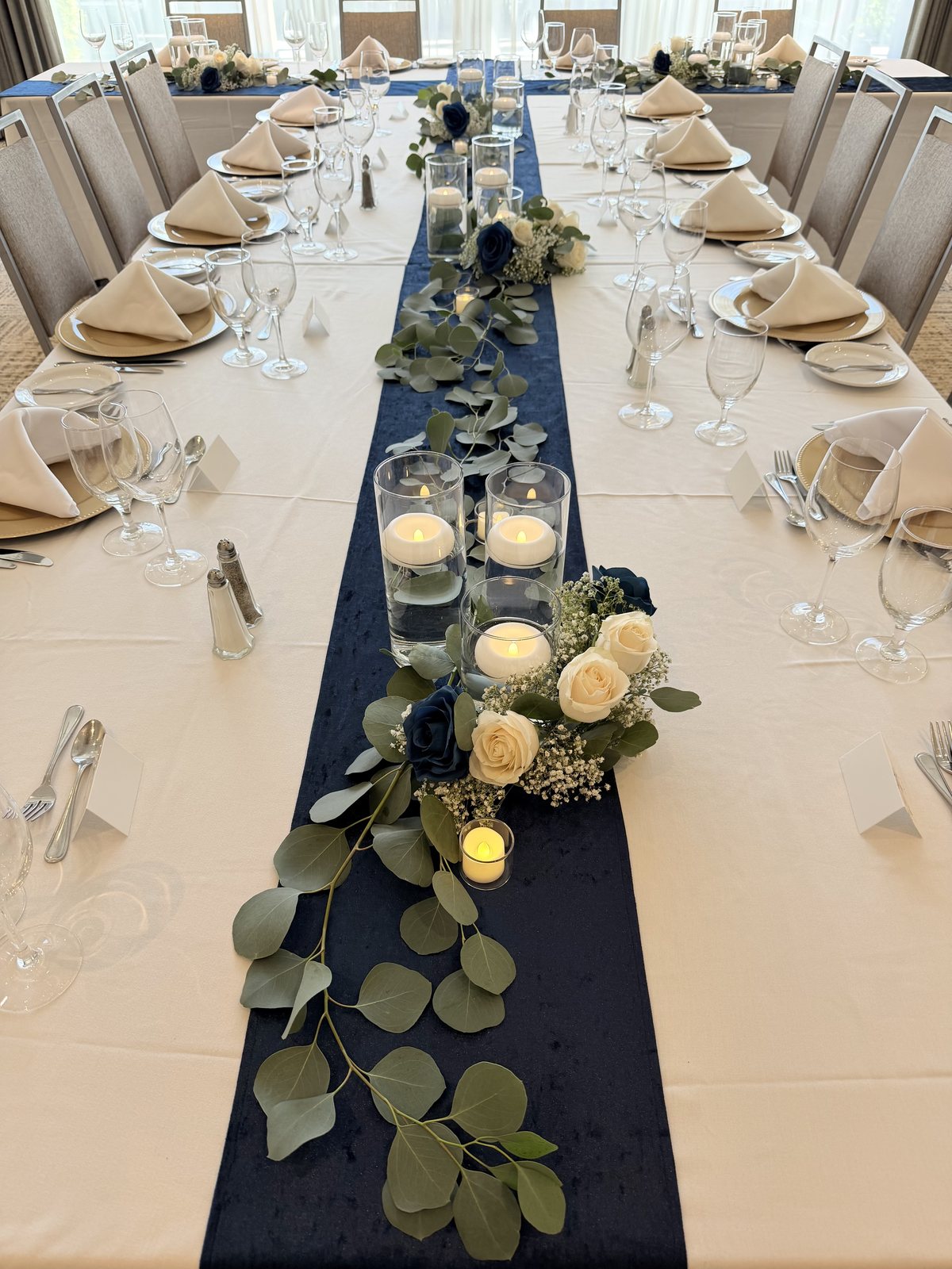 Wedding reception head table with a navy runner, eucalyptus, cream roses and candlelight at the Four Points by Sheraton Kelowna Airport