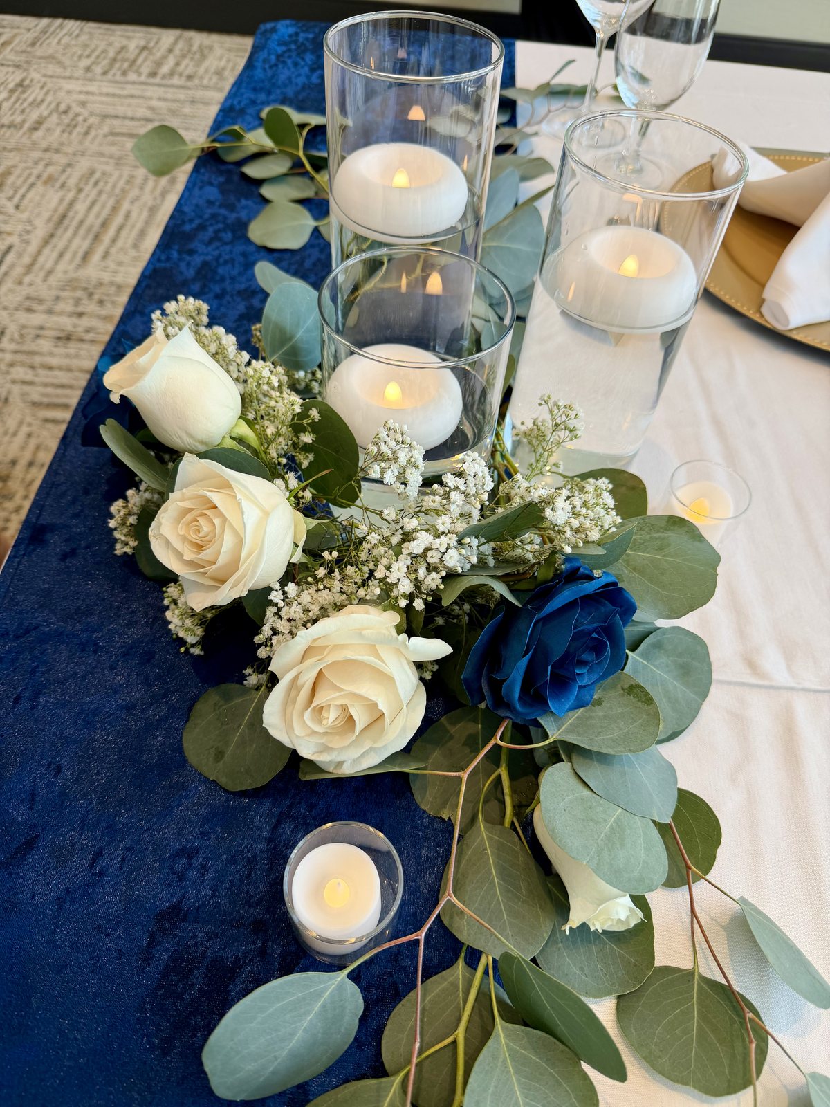 Reception table styled with a navy runner, cream roses, eucalyptus and candles — Four Points by Sheraton Kelowna Airport