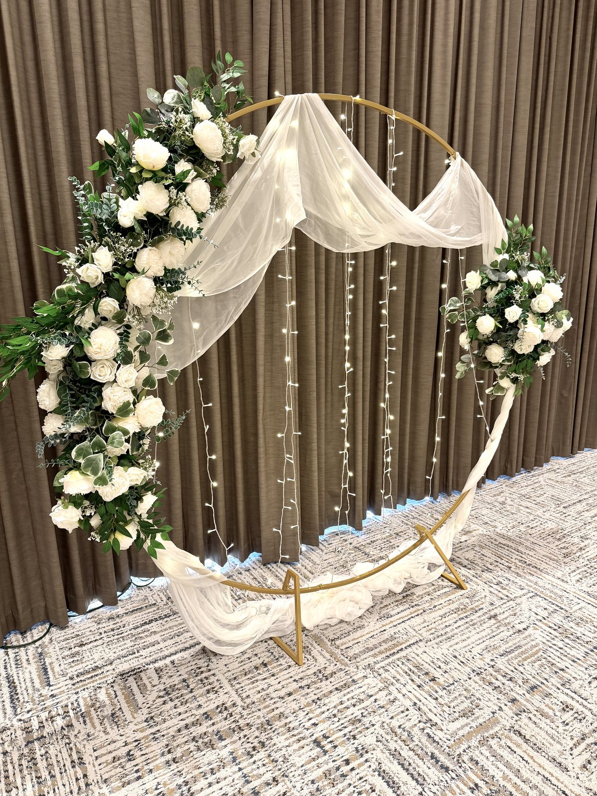 Circular moon-gate wedding arch with white roses, baby's breath, drape and fairy lights at the Four Points by Sheraton Kelowna Airport