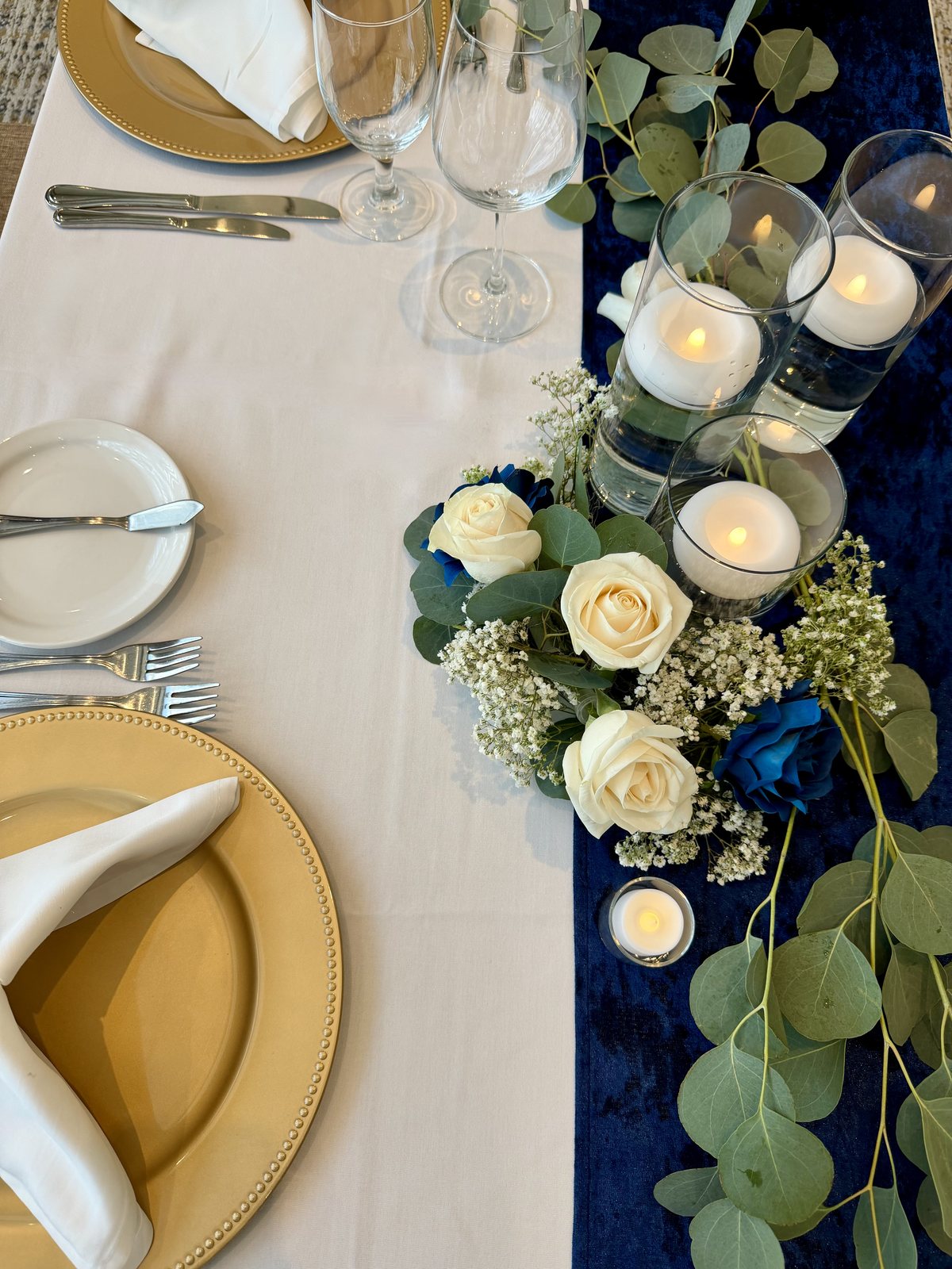 Wedding place setting with a gold charger, white napkin and cutlery on a navy runner — Four Points by Sheraton Kelowna reception