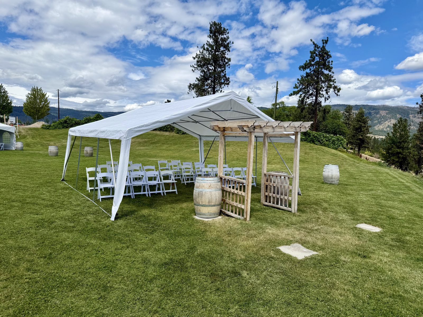Wedding ceremony under a frame tent with a wooden arch and wine barrels — Off The Grid Organic Winery
