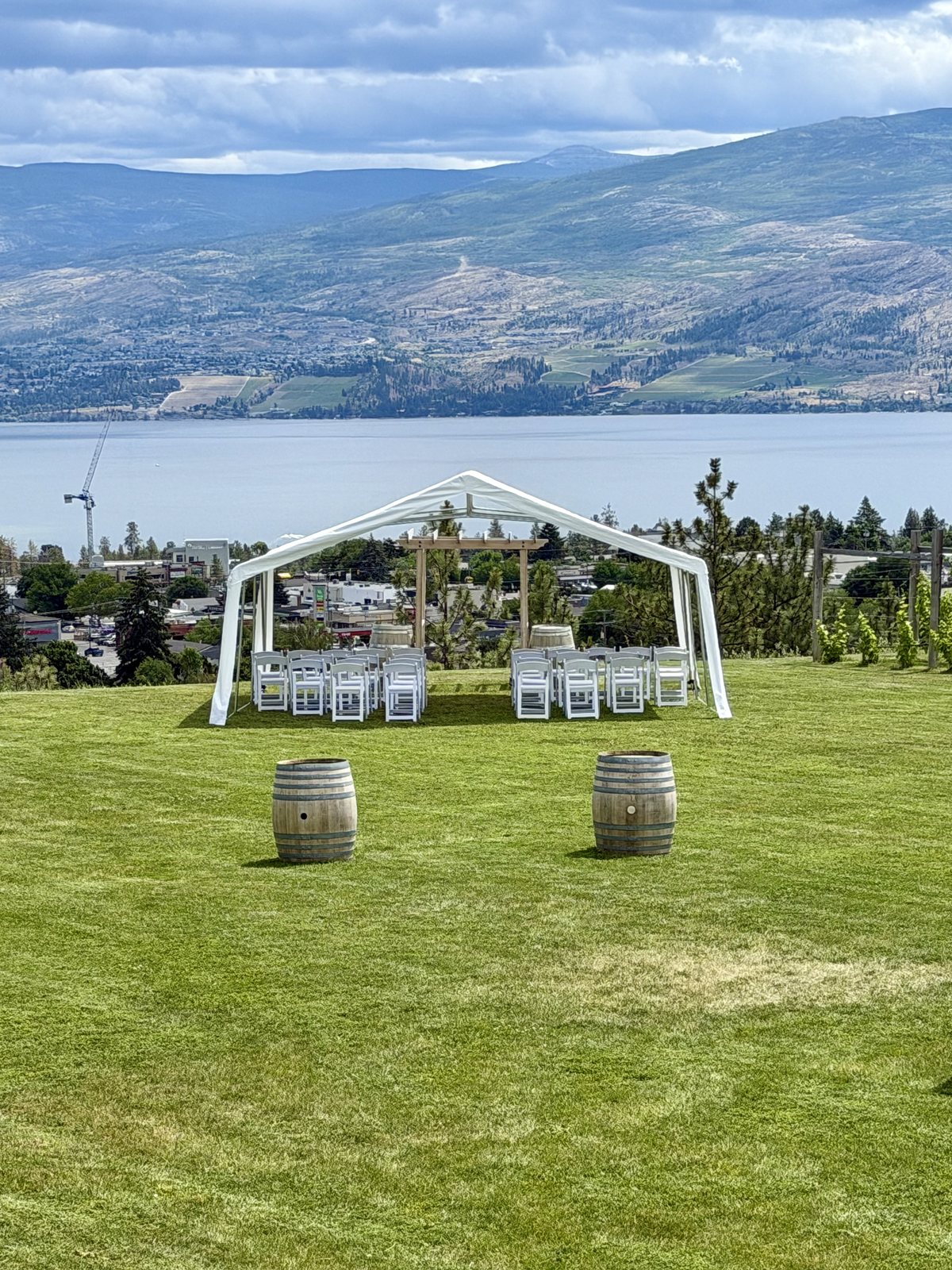 White frame tent wedding ceremony with wine barrels on the hillside at Off The Grid Organic Winery, West Kelowna, overlooking Okanagan Lake